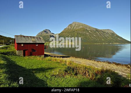 Hangar à bateaux en bois rouge à Lia avec l'île d'Aldra et les pics Hjarttinden derrière, au nord-ouest de la Norvège Banque D'Images