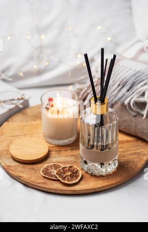 Parfum d'intérieur en bouteille en verre et bâtons de bambou avec bougie parfumée, livre en papier. Aromathérapie. Ambiance chaleureuse de la maison. Banque D'Images