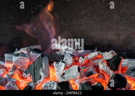 Photo de charbons chauds étincelants brûlant dans un fond de barbecue. Un gros plan de charbons de barbecue brûlants. Banque D'Images