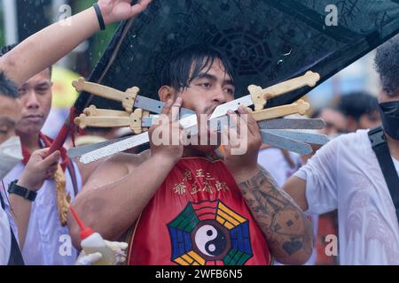 Pour le festival végétarien ou le festival des neuf empereurs à Phuket, en Thaïlande, un médium spirituel affiche une joue percée de plusieurs grandes épées Banque D'Images