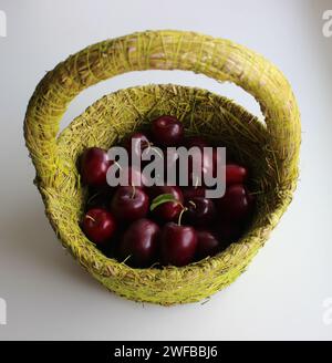 Panier de paille fait maison rempli de fruits de prune frais isolé sur blanc Banque D'Images