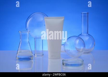 Un tube étiqueté vide placé au milieu, une boîte de Pétri, un erlenmeyer et des fioles florence à fond plat sont présentés. Fond bleu. Produit de beauté Banque D'Images