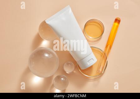 Tube blanc à étiquette vide placé sur des billes de verre et des boîtes de Pétri, tube à essai contenant des solutions orange. Production de produits cosmétiques de beauté en labat Banque D'Images