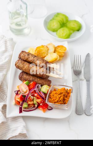 Saucisses traditionnelles du sud de l'europe sans peau cevapcici faites de viande hachée avec des pommes de terre cuites au four et une petite salade et trempette. Banque D'Images