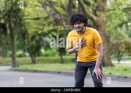 Jeune homme en t-shirt jaune ressentant des douleurs thoraciques tout en marchant dans le parc, exprimant l'inconfort et le concept de problème de santé Banque D'Images