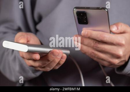 La main des hommes tiennent le téléphone et le chargeur, powerbank et le téléphone intelligent se connecte, l'énergie. Banque D'Images