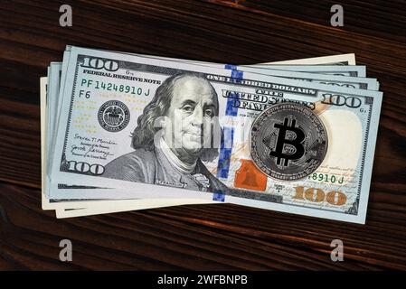 Pièce symbolique argent Bitcoin sur des billets de banque de cent dollars sur fond de bois. Échangez des bitcoins contre des dollars. Crypto-monnaie sur les États-Unis Banque D'Images
