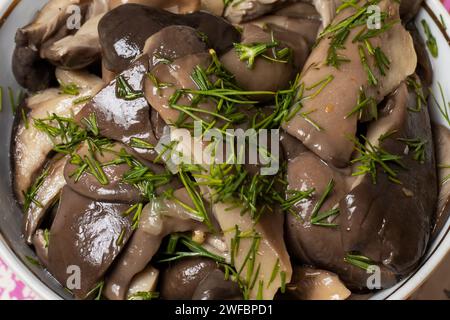 Champignons marinés dans un bol en céramique avec aneth. La serviette blanche ethnique frangée sur une table bleue. Suillus prêt à manger. Banque D'Images