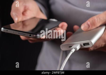 La main des hommes tiennent le téléphone et le chargeur, powerbank et le téléphone intelligent se connecte, l'énergie. Banque D'Images