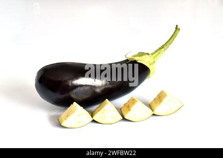 Sur un fond blanc, il y a un légume d'aubergine et plusieurs morceaux coupés d'une autre aubergine. Banque D'Images