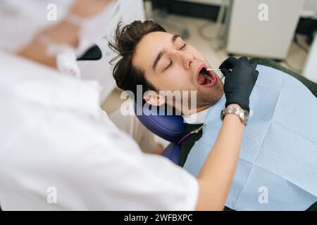 Vue de l'épaule d'une femme médecin méconnaissable prenant un test de salive de la bouche du patient mâle avec un coton-tige. Dentiste utilisant un coton-tige pour lubrifier Banque D'Images