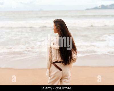 Solitude et sérénité : une belle femme profitant d'une promenade tranquille le soir d'été sur une plage de sable, contemplant le coucher de soleil vibrant sur l'océan Bleu. Banque D'Images