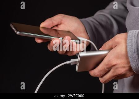 La main des hommes tiennent le téléphone et le chargeur, powerbank et le téléphone intelligent se connecte, l'énergie. Banque D'Images