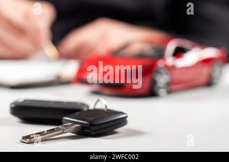 L'homme signe le document d'assurance automobile ou le papier de location. Signature écrite sur le contrat ou l'accord. Acheter ou vendre un véhicule neuf ou d'occasion. Touches de voiture sur l'onglet Banque D'Images