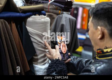 (240130) -- CHENGDU, 30 janv. 2024 (Xinhua) -- Nyima Wangden montre des vêtements pour costumes tibétains traditionnels à son client via un chat vidéo sur un marché de Chengdu, dans la province du Sichuan au sud-ouest de la Chine, le 5 janvier 2024. Nyima Wangden, un homme d'affaires tibétain originaire du comté de Heishui dans l'Aba Tibetan et de la préfecture autonome de Qiang dans le Sichuan, vit à Chengdu, la capitale provinciale, depuis plus de deux décennies. Nyima Wangden et son épouse Hoing Je, qui avaient tous deux hérité de leurs aînés de l'artisanat de la conception et de la fabrication de costumes tibétains traditionnels, ont exploité un magasin de vêtements spécialisés Banque D'Images