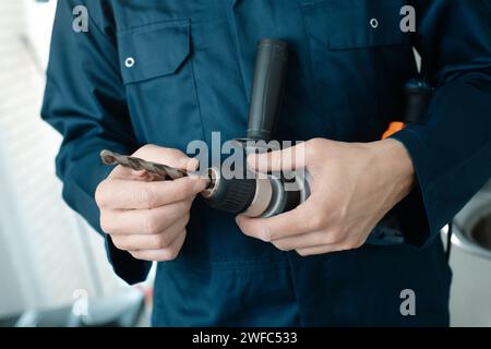 gros plan d'un homme caucasien, portant une combinaison bleue, mettant un foret en métal dans une perceuse électrique Banque D'Images