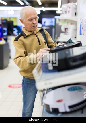 Senor homme retraité achetant aspirateur robotique dans la salle d'exposition du magasin d'appareils électriques Banque D'Images