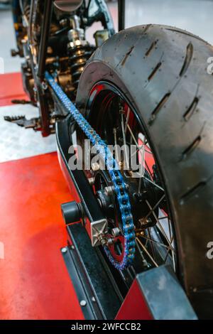 Gros plan de la roue arrière et de la chaîne bleue décorative sur moto personnalisée en usine Banque D'Images