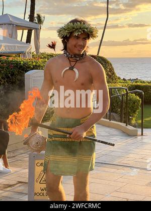 Un homme vêtu de vêtements traditionnels hawaïens tient et tient une coquille de conque et une torche enflammée au coucher du soleil au four Seasons Resort Maui à l'hôtel Wailea, Kihei, Hawaii, le 16 juillet 2023. Banque D'Images