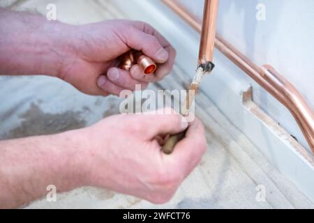 Un plombier préparant une tuyauterie en cuivre avec un flux à l'aide d'une petite brosse. L'ingénieur en chauffage utilisera de la soudure pour joindre deux tuyaux dans un chalumeau Banque D'Images