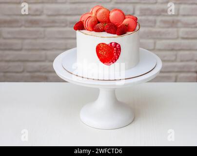 Beau gâteau blanc avec coeur rouge, macarons et fraise fraîche. Un cadeau doux pour la Saint-Valentin, pour la célébration de mariage ou pour anniversa romantique Banque D'Images