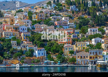 SYMI, GRÈCE - 3 JUILLET 2022 : Port de Symi, avec des demeures néoclassiques colorées couvrant les pentes près de la ville principale. Une partie de l'île du Dodécanèse. Banque D'Images