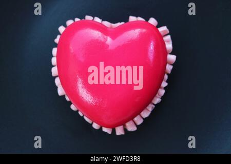 Vue de dessus du gâteau en mousse aux fraises en forme de cœur rose vibrant isolé sur plaque noire Banque D'Images