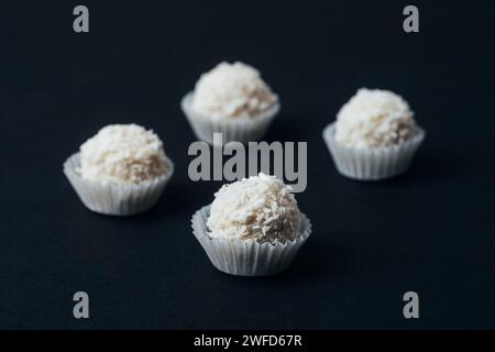 Bonbons à la noix de coco dans des gobelets en papier sur la table noire. Gros plan. Banque D'Images