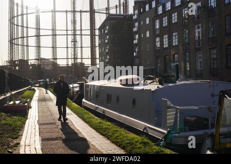 Un homme marche le long de la voie de remorquage près du Regent's Canal au soleil d'hiver tôt le matin. Les bateaux de maison sont amarrés tout le long du côté du canal. Banque D'Images