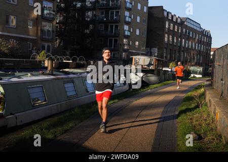 Deux hommes font de l'exercice en courant le long du Regent's Canal au soleil matinal de l'hiver. Les bateaux de maison sont amarrés tout le long du canal. Banque D'Images