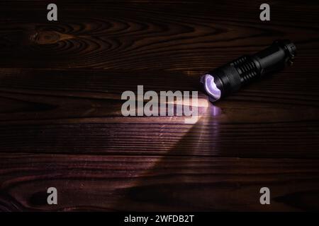 Lampe de poche et faisceau de lumière dans l'obscurité. Une lampe LED moderne avec projection lumineuse sur une table en bois sombre. Surface avec espace de copie. Banque D'Images