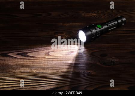 Lampe de poche et faisceau de lumière dans l'obscurité. Une lampe LED moderne avec projection lumineuse sur une table en bois sombre. Surface avec espace de copie. Banque D'Images