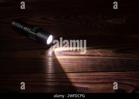 Lampe de poche et faisceau de lumière dans l'obscurité. Une lampe LED moderne avec projection lumineuse sur une table en bois sombre. Surface avec espace de copie. Banque D'Images