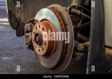 Ancien disque de frein avant avec étrier et plaquettes de frein dans la voiture, sur un ascenseur de voiture dans un atelier, gros plan d'un étrier de frein Banque D'Images