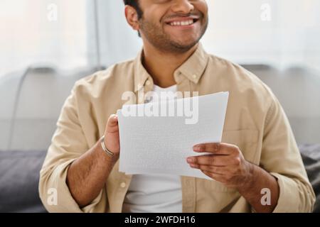 homme aveugle indien joyeux dans une tenue confortable décontractée assis sur un canapé et lisant le code braille Banque D'Images