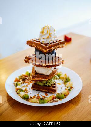 Gaufres, gaufre ou wafel ou gaufres avec fruits, glace et garniture. Un plaisir sucré. Gaufre à la crème glacée fraîchement cuite avec de délicieuses garnitures sur bois Banque D'Images