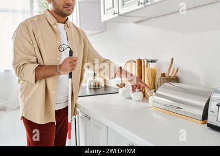 vue recadrée d'un homme indien handicapé dans des vêtements de maison tenant le bâton de marche tout en préparant la nourriture, aveugle Banque D'Images