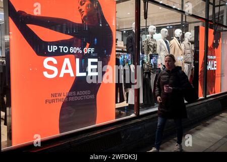 Le 17 janvier 2024 à Londres, au Royaume-Uni, les gens qui font du shopping sur Regent Street passent devant de grands panneaux de vente de janvier en rouge pour les grands magasins de détail de vêtements de rue. Son temps pour les soldes d'hiver, et la plupart des magasins annoncent de grandes réductions de prix. Regent Street est un important centre de vente au détail dans le West End de la capitale et est connu pour ses magasins de détail phares, dont la majorité sont des magasins de mode et de vêtements haut de gamme. Banque D'Images