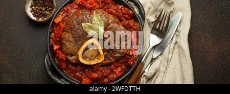 Plat traditionnel italien Ossobuco tous milanais fait avec de la viande de jarret de veau coupé avec sauce tomate aux légumes servi dans une casserole noire vue de dessus sur Banque D'Images