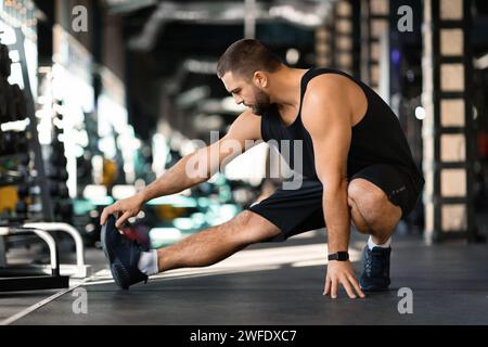Beau jeune homme effectuant l'étirement des jambes avant l'entraînement dans la salle de gym Banque D'Images