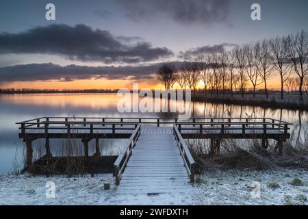 Jetée au bord du lac Dirkshorn dans un cadre hivernal. Une averse de neige pendant la nuit crée un paysage blanc au lever du soleil. Une averse de neige à l'horizon. Banque D'Images