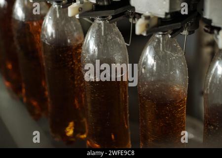 Plusieurs bouteilles en plastique accrochées au convoyeur à bande ou à la chaîne d'assemblage pendant le processus de remplissage de soda ou de limonade avant l'emballage Banque D'Images