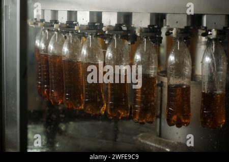 Rangée de plusieurs bouteilles en plastique transparent accrochées sur le convoyeur à bande pendant le processus de versement de soude ou de limonade avant l'emballage Banque D'Images