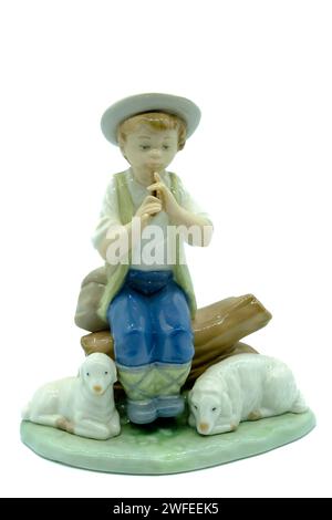 Figure antique en porcelaine d'un berger garçon jouant du sifflet ou des tuyaux assis sur une bûche avec deux moutons ou agneaux à ses pieds. Banque D'Images