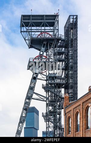 Un puits de levage de mine contre un ciel nuageux. Gratte-ciel de bureaux modernes en arrière-plan, vieux bâtiments en briques au premier plan Banque D'Images