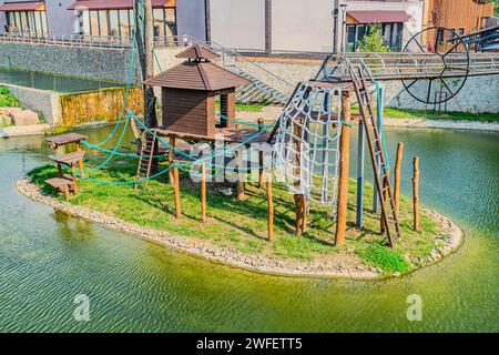 Activités de jeux pour enfants colorés dans un parc public entouré d'un étang vert au coucher du soleil course pour enfants, toboggans, balançoires sur une aire de jeux moderne. Neighbo urbain Banque D'Images