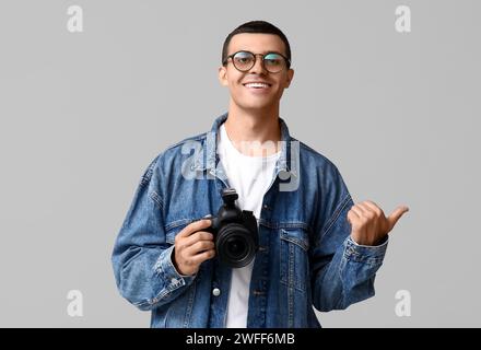 Photographe masculin avec appareil photo moderne pointant vers quelque chose sur fond gris Banque D'Images