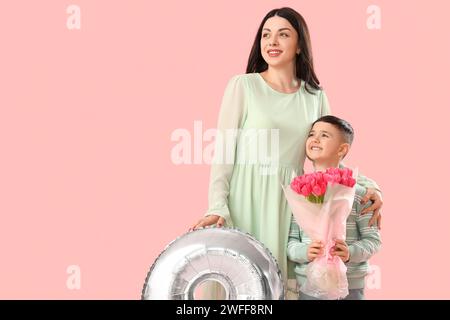 Mignon petit garçon avec sa mère tenant bouquet de tulipes et ballon d'air sur fond rose. Journée internationale de la femme Banque D'Images