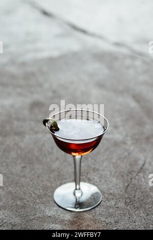 cocktail élégant de couleur ambre en verre à bordure dorée vintage, rétro-éclairé sur le sol en béton avec de l'huile visible sur le dessus de la boisson Banque D'Images