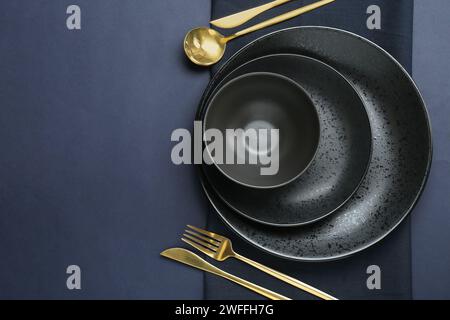 Assiettes en céramique élégantes, bol, couverts et serviette sur fond bleu foncé, vue de dessus. Espace pour le texte Banque D'Images